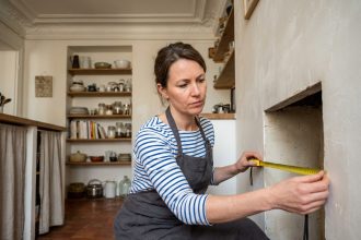 Femme mesurant une niche murale dans une cuisine ancienne d'un appartement nantais pour optimiser l'espace de rangement