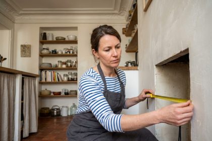 Femme mesurant une niche murale dans une cuisine ancienne d'un appartement nantais pour optimiser l'espace de rangement